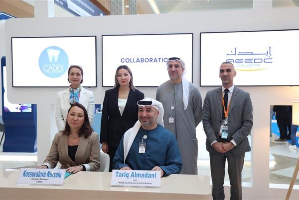 A group of six professionals pose for a photograph at the signing ceremony of a collaboration agreement between AEEDC Dubai and CADEX. Two key representatives, Kossuvalova Nursulu, General Manager of CADEX, and Tariq Almadani, CEO of INDEX Conferences & Exhibitions, are seated at the signing table, smiling. The background features digital screens displaying the logos of CADEX and AEEDC Dubai with the word "Collaboration" in between.