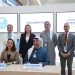 A group of six professionals pose for a photograph at the signing ceremony of a collaboration agreement between AEEDC Dubai and CADEX. Two key representatives, Kossuvalova Nursulu, General Manager of CADEX, and Tariq Almadani, CEO of INDEX Conferences & Exhibitions, are seated at the signing table, smiling. The background features digital screens displaying the logos of CADEX and AEEDC Dubai with the word "Collaboration" in between.